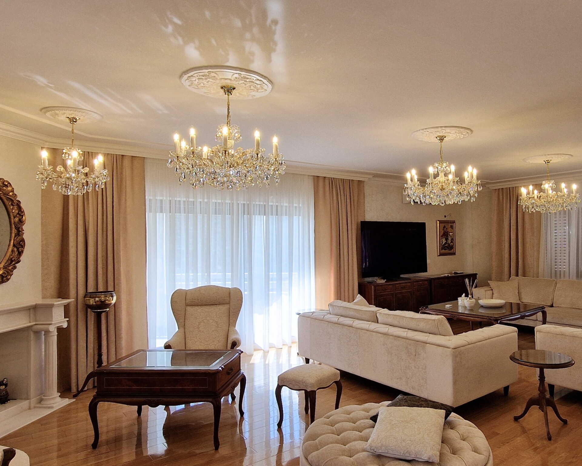 Salón con lámparas de araña de cristal, sofás color crema y chimenea