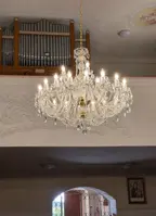 Gran lámpara de cristal en acabado dorado colgada en una iglesia con órgano y decoración de estuco
