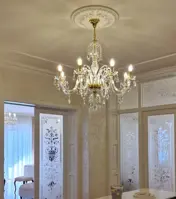 Lámpara de cristal con ocho brazos en acabado dorado colgada en un interior de lujo con puertas de cristal grabado
