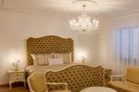 Lámpara de cristal María Teresa en acabado dorado sobre una cama con cabecero tapizado en un interior clásico