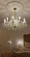Lámpara de cristal María Teresa en acabado dorado colgada en un dormitorio de lujo con muebles tapizados