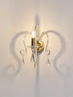 Aplique de cristal encendido con un brazo y colgantes sobre una pared blanca
